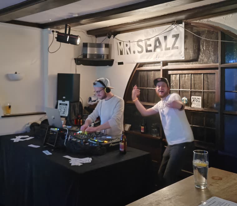 Flo an den Decks, Dave daneben, unter einem Mr.-Sealz-Banner.